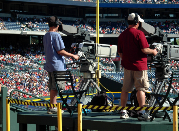 Two people behind large video cameras at a sporting event